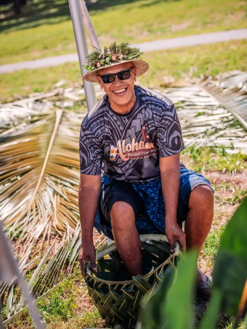 Smiling island villager weaving coconut palm fronds at a luau activity station